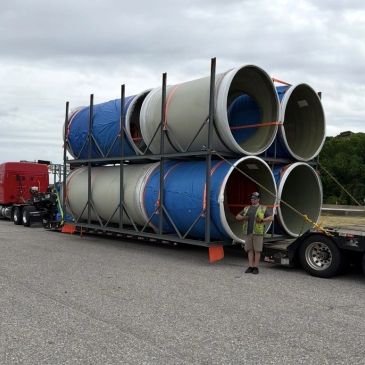 Large cylindrical structures loaded on a flatbed truck with a worker standing beside them.