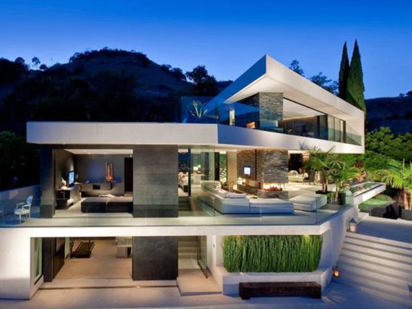 Modern luxury house with glass walls and outdoor greenery at dusk.