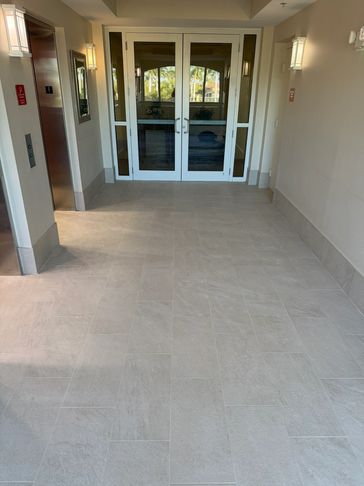 Clean tiled floor in a well-lit hallway with white double doors and an elevator.