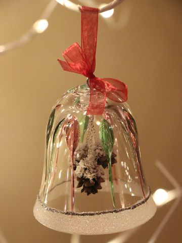 Glass bell ornament with red ribbon and pinecone inside.