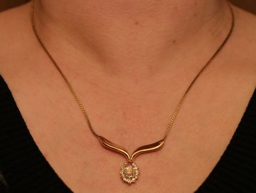 Golden necklace with a pendant on a person's neck.