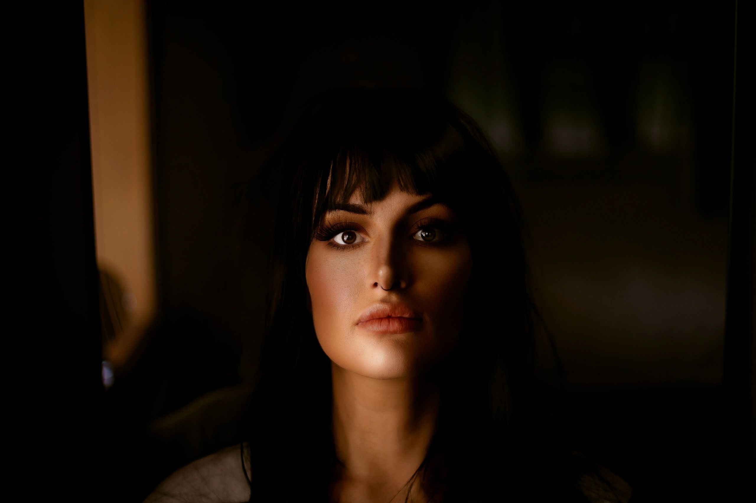 Close-up portrait of a woman with dark hair and striking eyes in low light.
