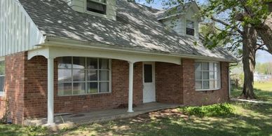 Brick house with white columns and large windows on a sunny day.