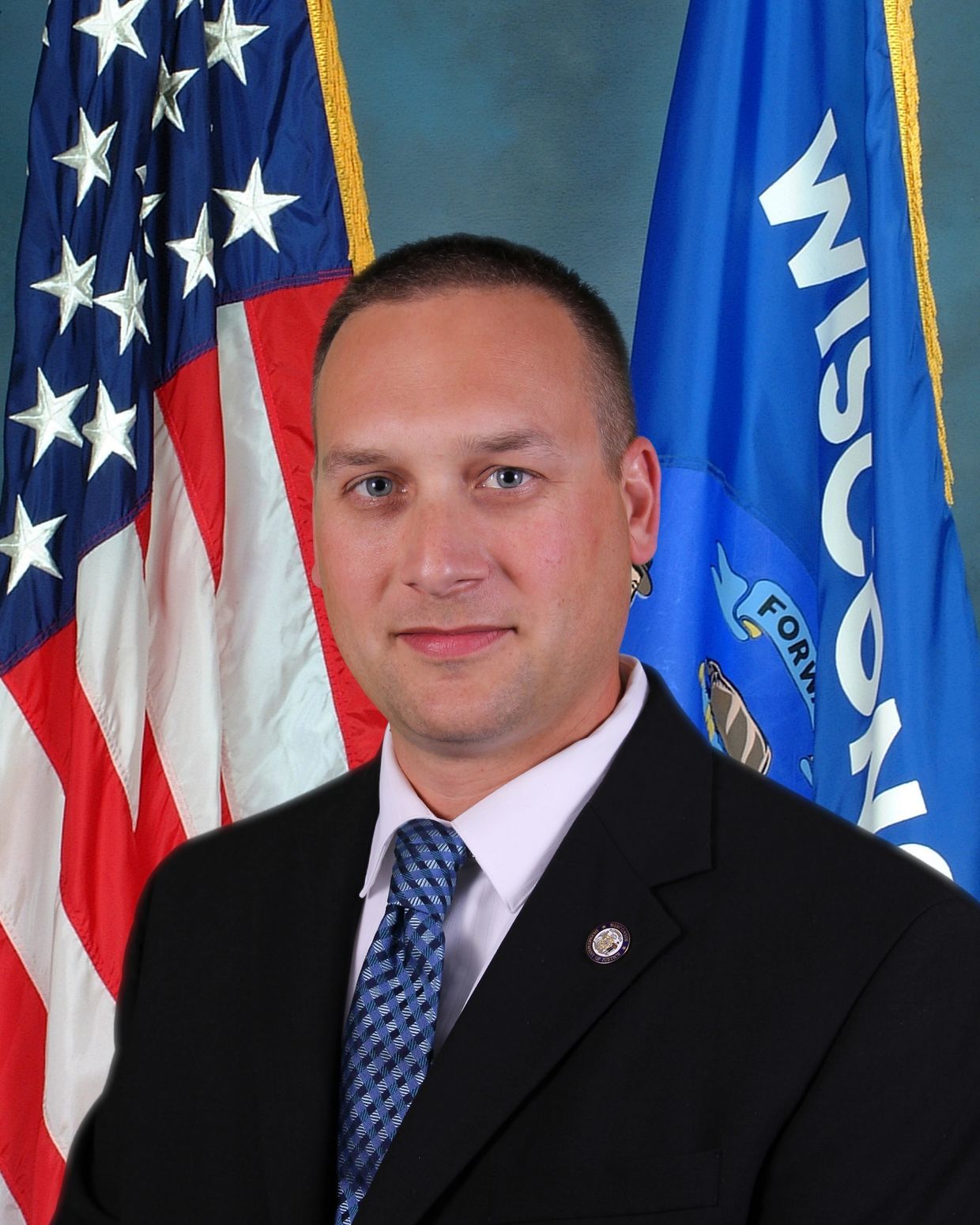 Professional portrait of a man in a suit with American and Wisconsin flags.