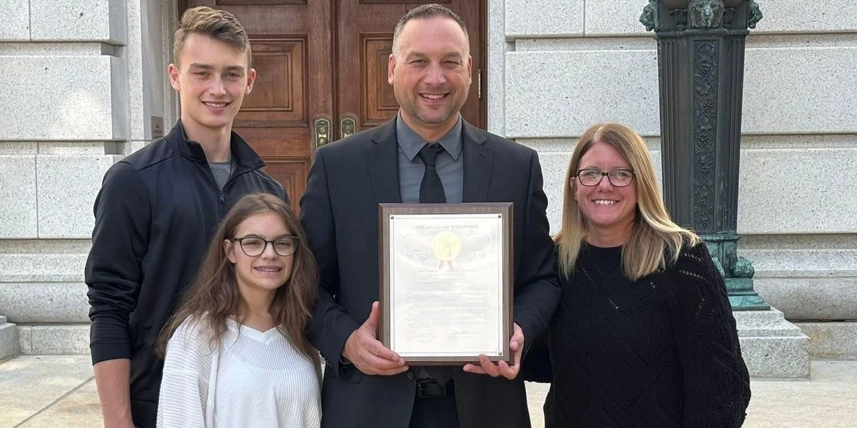 A family posing outside a formal building with a certificate.