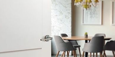 White modern interior door with metal handle opening to a stylish dining area with chandelier.