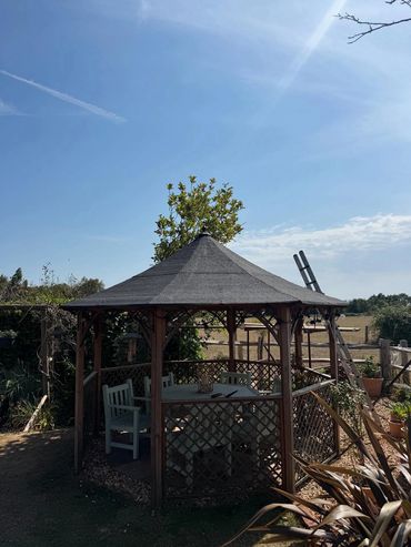 A wooden gazebo with chairs and a table under a clear blue sky.