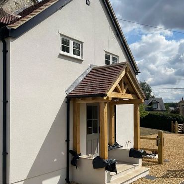 Newly built porch with timber frame and tiled roof on a white house.