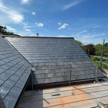 Newly installed grey slate roof under a bright blue sky.