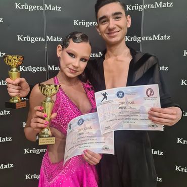 Two dancers holding trophies and diplomas, smiling.