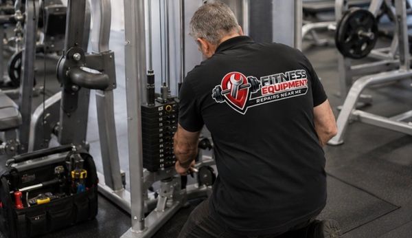 Technician repairing gym equipment in a fitness center.