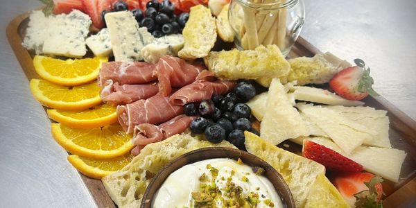 A colorful charcuterie board with meats, cheeses, fruits, and dips.
