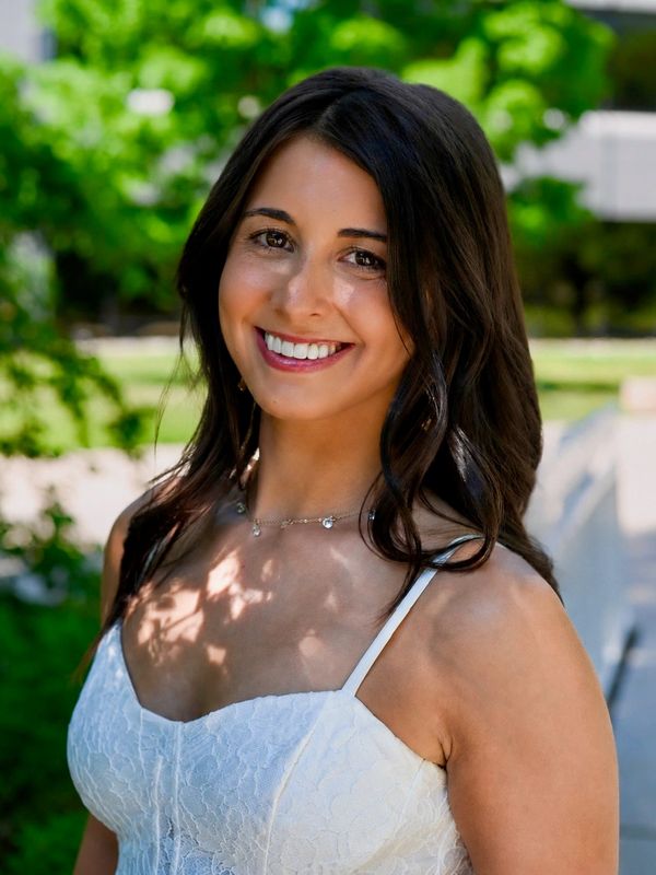 Smiling woman in a white dress outdoors.