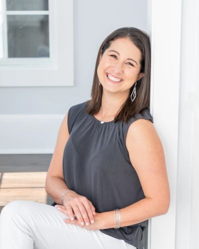 Smiling woman sitting and leaning against a wall.