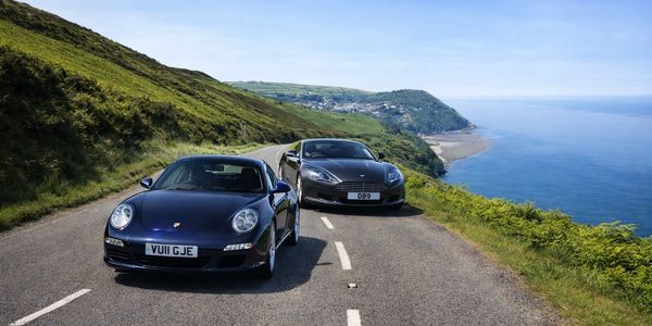 porsche and aston martin on coastal road in convoy