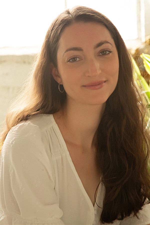 A woman with long brown hair wearing a white blouse smiles softly.