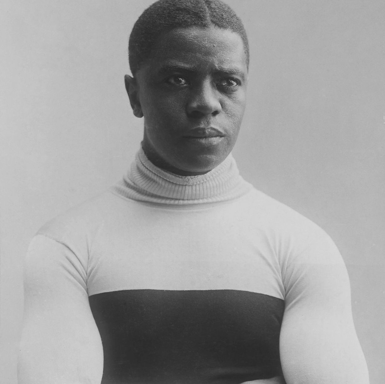 Black and white portrait of a strong man with arms crossed, wearing a turtleneck sweater.