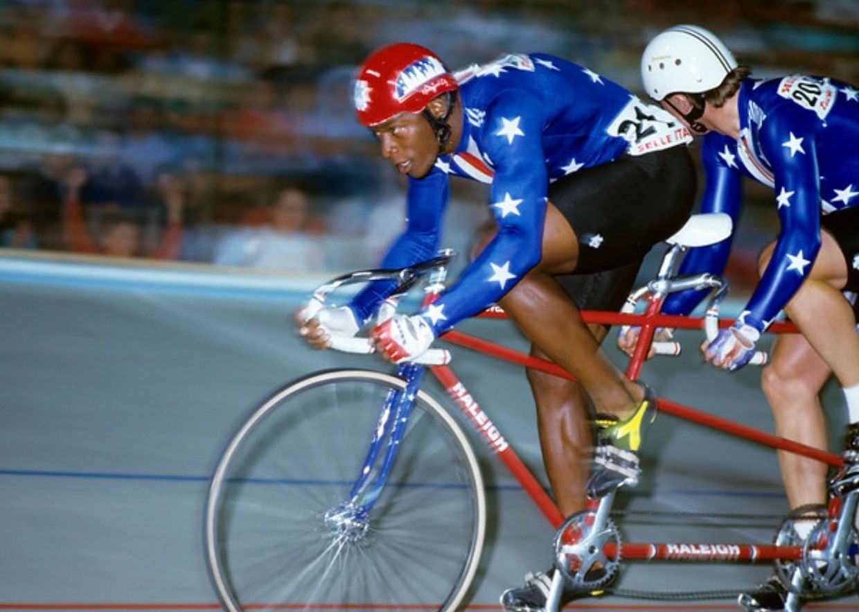 Two cyclists in blue star-spangled suits racing on a tandem bike.