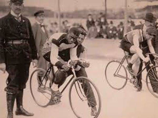 Vintage black-and-white photo of cyclists racing with a policeman nearby.