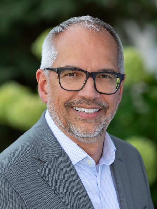 Smiling mature man with glasses in a gray suit outdoors.