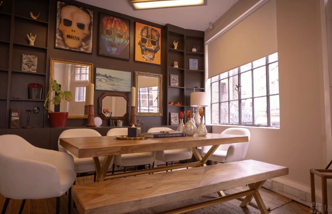 Modern dining room with wooden table, white chairs, and skull art on dark wall.