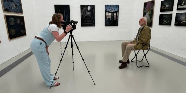 Woman filming an elderly man in an art gallery.