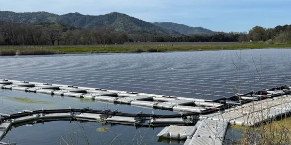 Solar panels floating on a serene lake with mountains in the background.