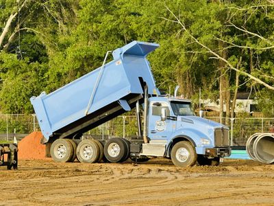 Light blue dump truck unloading dirt at a construction site.