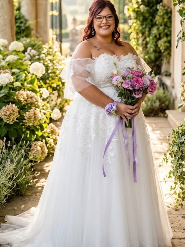 Smiling bride in a white gown holding a purple bouquet in a garden setting.