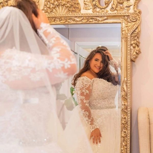 Bride admiring herself in a large ornate mirror, smiling happily.