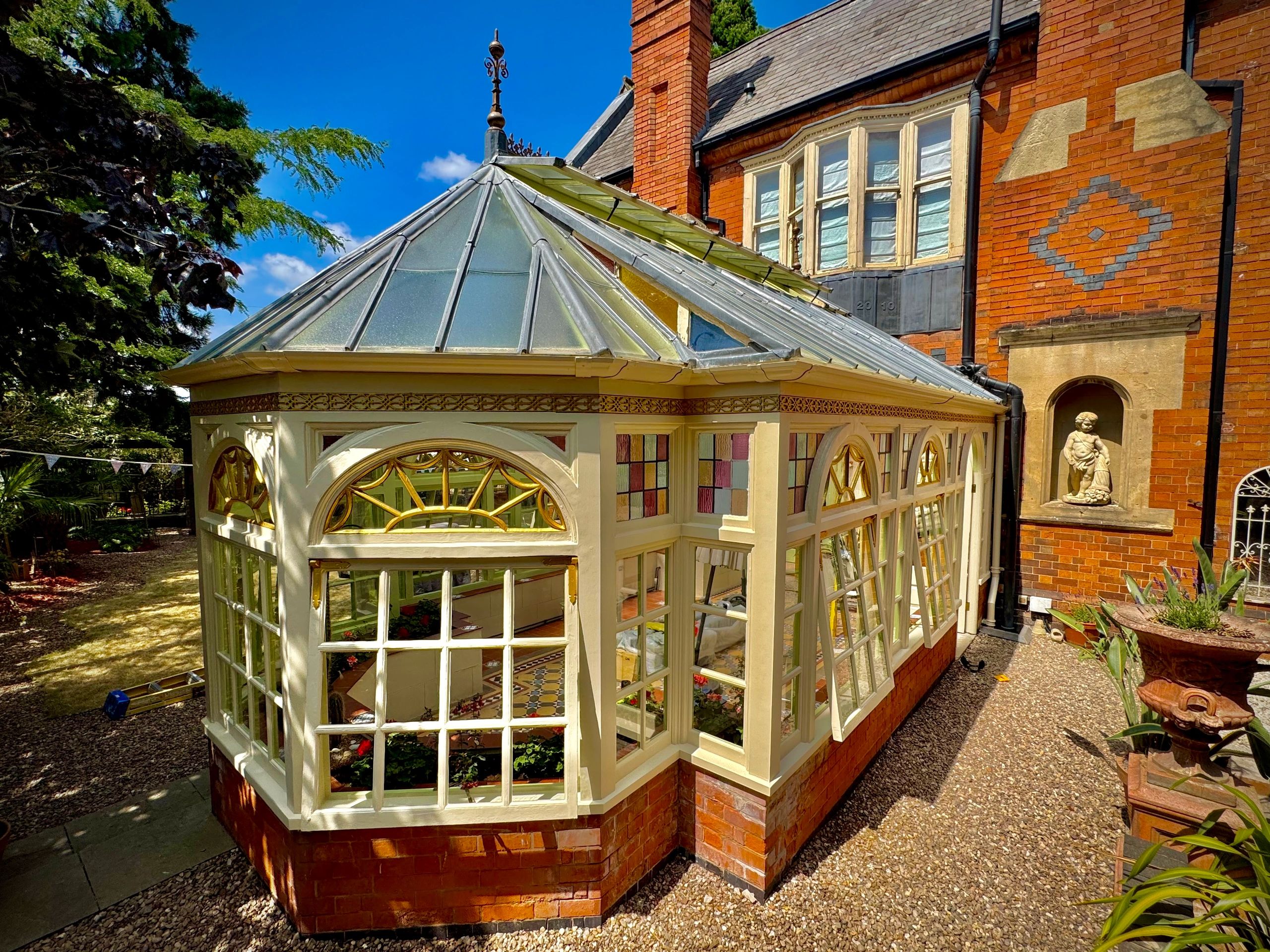 Glass conservatory attached to a red brick house on a sunny day.