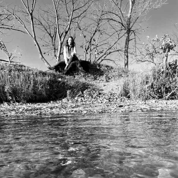 A woman sitting on a rock by a calm water body surrounded by trees.
