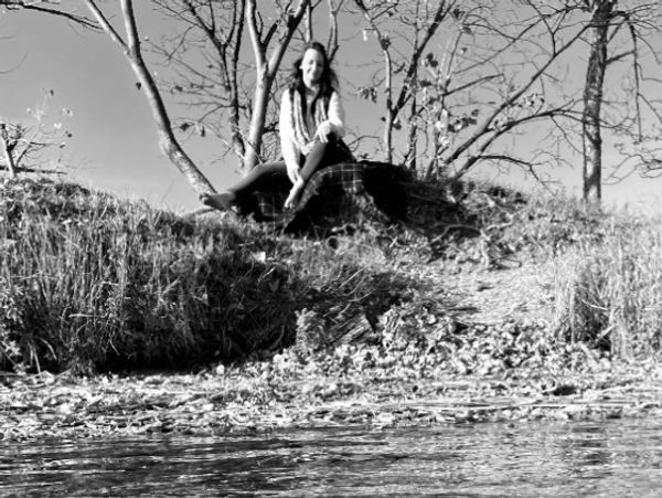 A woman sitting on a rock by a calm water body surrounded by trees.