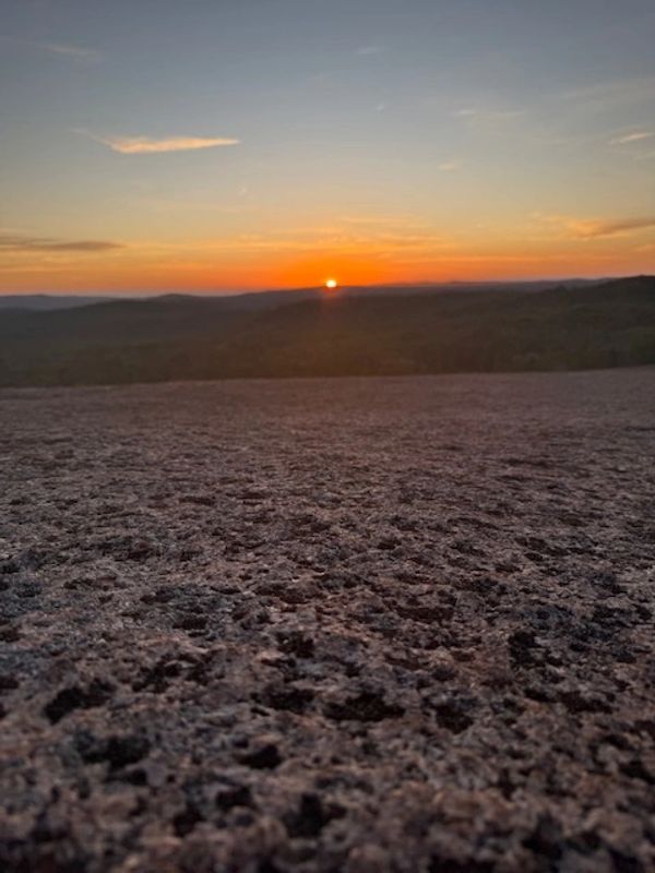 Sunset over rocky terrain with distant hills under a colorful sky.