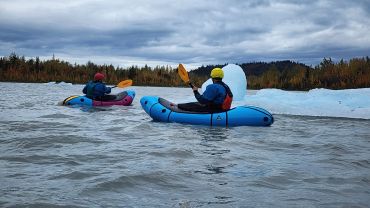Two people kayaking on a cold lake with icy surroundings.