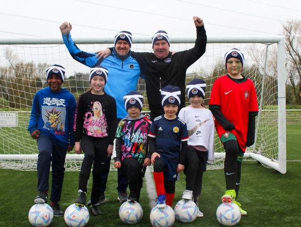 A diverse group of children and two adults pose on a soccer field with soccer balls.