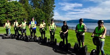 Group of people riding Segways near a lake on a sunny day.