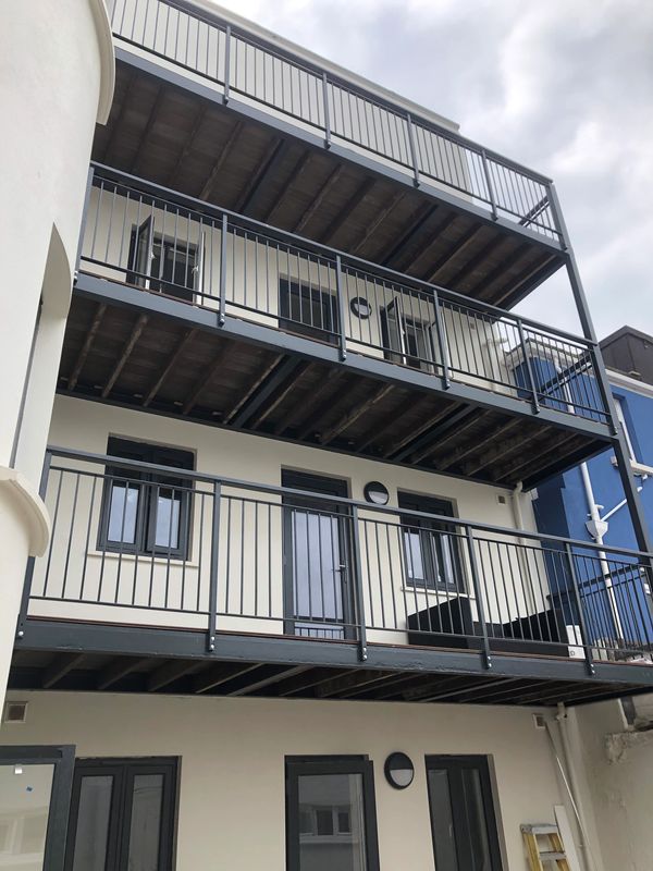 Modern building with three iron-railed balconies under a cloudy sky.