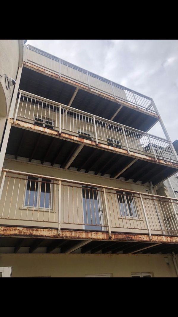 Rusty metal balconies on a three-story building under a cloudy sky.