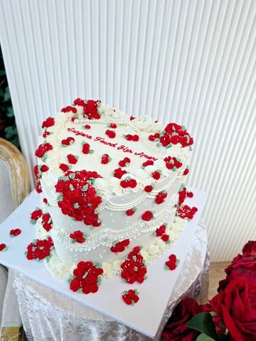 Heart-shaped white cake decorated with red flowers.