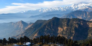 Snowy mountain range with trees and hills in the foreground.
