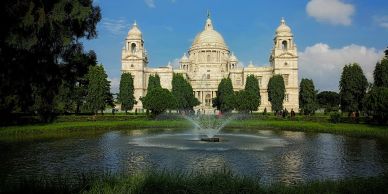 A grand historic building behind a pond with a central fountain.