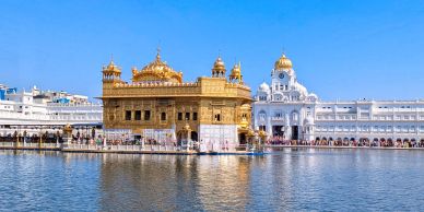 The Golden Temple reflected in the water under a clear blue sky.