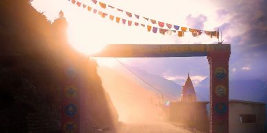 Sunlit entrance arch with prayer flags and mountainous background.