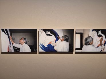 Three photos show an artist painting a large mural with a bird design indoors.