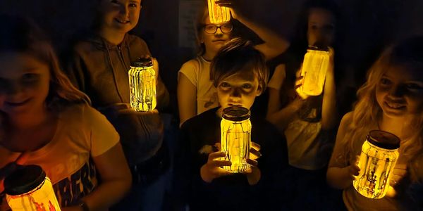 Children holding glowing jars in the dark.