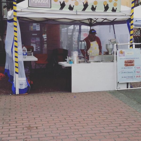 Vendor selling mini donuts at a market stall under a white tent.