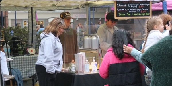 People shopping and interacting at an outdoor market stall with hand sanitizers.