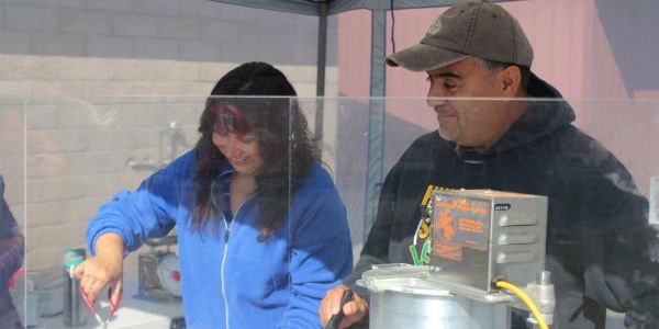 Two people preparing food behind a protective screen at a stall.
