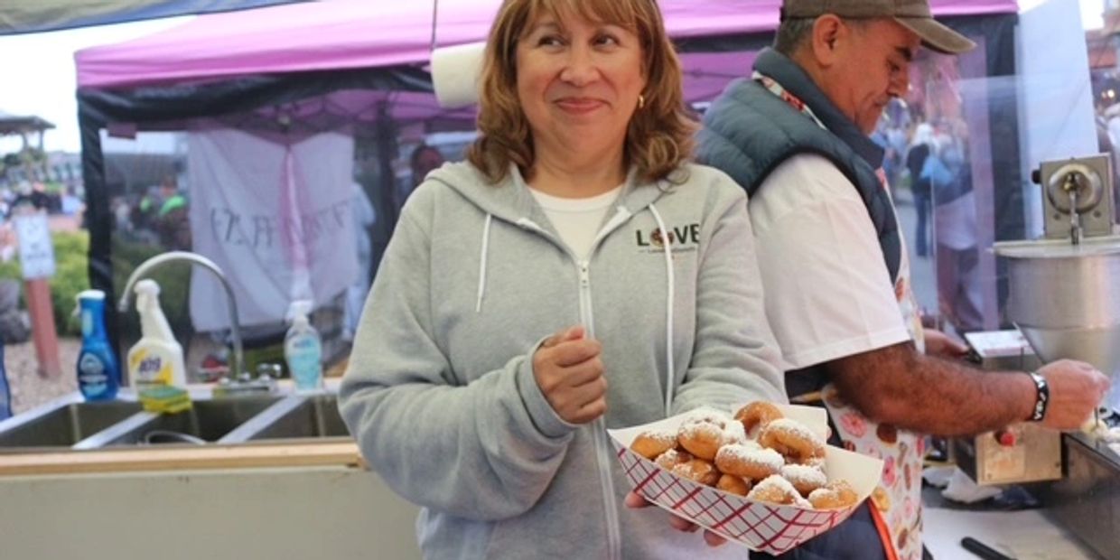 Woman holding a tray of powdered sugar donuts at a food stall.